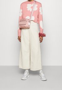 Rosa tröja med vitt blommönster, vita vidbyxor och en ljusrosa crossbody-väska. Grå sneakers med vita accenter.