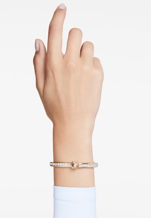 Goldfarbene Armbanduhr mit einem hexagonalen Zentrum, das eine Reihe von klaren Kristallen entlang des Armbands aufweist. Glatte Textur, minimalistisches Design.