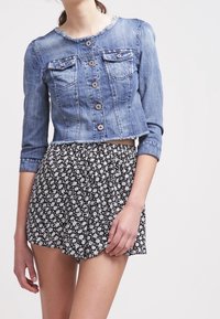 Žena v krátkém džínovém saku s knoflíky a třičtvrtinovými rukávy, doplněná černobílými květinovými šortkami.