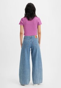 Strak zittend, roze cropped top met geplooide stof en korte mouwen, gecombineerd met hooggetailleerde, wijd uitlopende blauwe denim jeans met een leren merklabel.