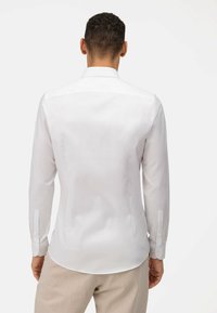 Witte shirt met lange mouwen, een gestructureerde kraag, een gladde textuur, knopen bij de mouwen en een afgeronde zoom. De achterkant toont een strakke lijn en een getailleerde pasvorm.