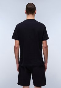 Black cotton T-shirt with short sleeves, crew neck, and a relaxed fit. Worn with matching black shorts, smooth texture, no visible patterns.