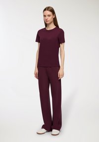 Burgundowy t-shirt z krótkim rękawem w połączeniu z luźnymi spodniami w tym samym kolorze, wykonanymi z miękkiego materiału o gładkiej fakturze. Na nogach casualowe białe trampki.