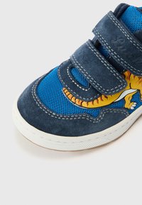 Tumši zils zamša sporta apavu ar ziliem tīkla paneļiem, baltu gumijas zolīti un Velcro siksnām. Sānos rotāts ar dzeltenu dinozaura grafiku.