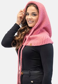 Cappuccio rosa lavorato a maglia con un design a coste, caratterizzato da una lunga frangia, indossato sopra una maglietta nera. Include un piccolo dettaglio con etichetta sul lato.
