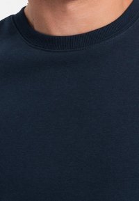 Marinblå bomullströja med ribbad rund halsringning och slät yta, utan synliga mönster eller detaljer i metall.