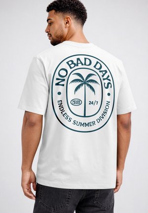 Mann trägt weißes T-Shirt mit großem dunkelblauem Palmenmotiv und Aufdruck „NO BAD DAYS“, „NEVER LESS“, „24/7“ und „ENDLESS SUMMER DIVISION“ auf dem Rücken.
