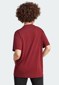 Camiseta de manga corta burdeos con un corte relajado, fabricada en un tejido suave y con escote redondo, que presenta una textura lisa y sin patrones visibles.