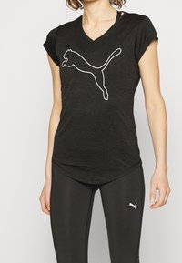 Svart, kortärmad träningsskjorta med V-ringning; har en vit Puma-logotyp. Bärs med svarta leggings som visar upp en åtsittande design och mjuk textur.