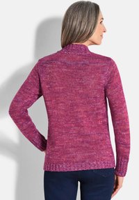 Pull en tricot avec des teintes chinées de rose, présentant un col montant et des manches longues, avec des poignets et un ourlet côtelés, texture douce.
