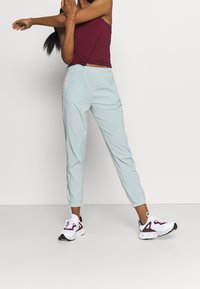 Light blue athletic joggers feature an elastic waistband and cuffs, with contrasting pink accents. Paired with a maroon tank top and white sneakers.