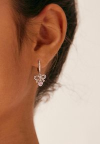 Pendiente de aro de plata con un diseño de lazo y un acento de gema rosa. Presenta un acabado elegante y un mecanismo de cierre simple.