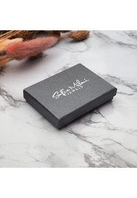 Sort tekstureret smykkeboks med en glat finish, prydet med et hvidt logo, rektangulær form og let glans. Placeret på en marmoryt.
