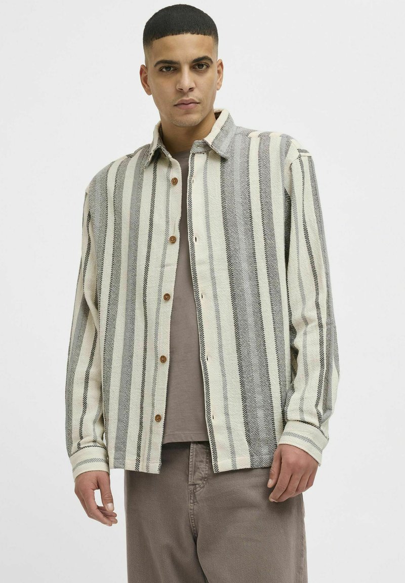 Camisa abotonada con rayas verticales en crema, gris y negro, con cuello desplegable, mangas largas y botones de madera.