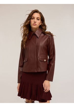 Burgunderfarbene Lederjacke mit spitzem Kragen, Reißverschluss und Fronttaschen; kombiniert mit einem plissierten burgunderfarbigen Rock. Glatte Textur.