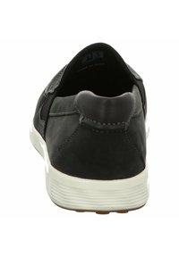 Scarpa nera in pelle scivolosa con una texture liscia, suola bianca a profilo basso e dettagli di cucitura sottili sulla parte superiore.
