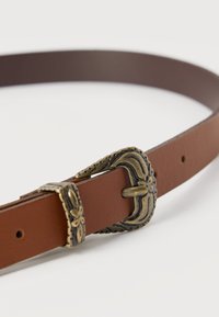 Καφέ δερμάτινη ζώνη με περίτεχνη, παλαιωμένη, χρυσαφένια αγκράφα με λουλουδένιο σχέδιο και αντίστοιχο θηλάκι σε λευκό φόντο.