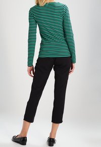 Grün- und schwarzgestreiftes Langarmshirt mit Rundhalsausschnitt, kombiniert mit schwarzen, knöchellangen Hosen und getragen mit schwarzen Ballerinas. Figurbetonter Schnitt, gerippte Textur.