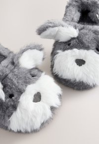 Graue flauschige Hausschuhe, die einem Hund ähneln, mit weißen Akzenten, runden Ohren und einer strukturierten Nase. Weiches Material und kuscheliges Design.