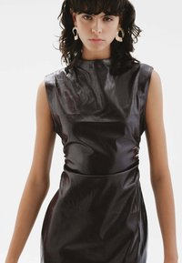 Vestido sin mangas de cuero sintético negro con cuello alto, silueta ajustada y un brillo sutil. Cuenta con una textura suave y detalle de fruncido lateral.