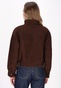 Brun suede jakke med høj krave, oversized pasform og sidelukninger. Samlet med mørkeblå denim jeans, der viser enkle syningsdetaljer.