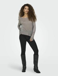 Maglione grigio a maniche lunghe con vestibilità rilassata, abbinato a jeans skinny neri e stivali neri alti fino al ginocchio. L'outfit presenta un design minimalista.