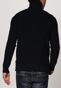 Suéter de punto de cuello alto en azul marino oscuro con puños y dobladillo acanalados, hecho de material suave; presenta un diseño ajustado y un cuello alto.