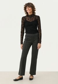 Zwarte kant lange mouwen top over een mouwloze body, gecombineerd met grijze gestreepte flared broek en zwarte ballerina's. Licht, gestructureerde stof.