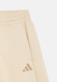 Μπεζ φόρμα με ελαστική μέση, με απαλό ύφασμα και μικρό, τονικό λογότυπο adidas στην αριστερή πλευρά.