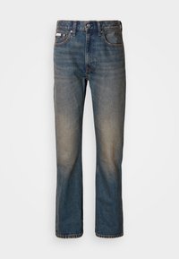 Vaqueros de tiro alto en denim azul, con un diseño de pierna recta, parches desgastados y descoloridos, y un estilo tradicional de cinco bolsillos.