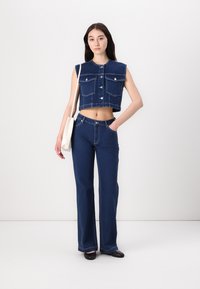 Gilet in denim tagliato con grandi tasche e bottoni argentati abbinato a jeans a campana blu scuro a vita alta. Tessuto liscio con cuciture pulite.