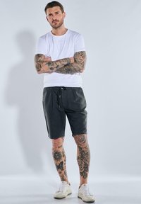 Dark gray shorts with a drawstring waist, combined with a plain white t-shirt. Features visible tattoos on arms and legs. White sneakers.