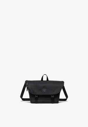 Black messenger bag made of durable fabric; features a flap closure, adjustable strap, top handle, and front logo patch.