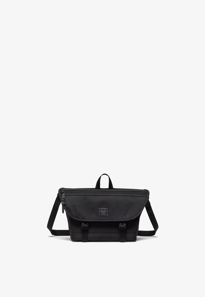 Black messenger bag made of durable fabric; features a flap closure, adjustable strap, top handle, and front logo patch.