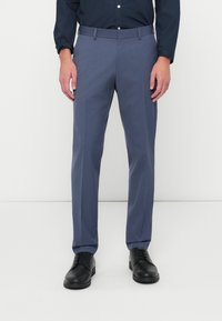 Γκρι παντελόνι από μαλακό ύφασμα, με στενή γραμμή, επίπεδο μπροστινό μέρος και δύο πλαϊνές τσέπες, συνδυασμένο με μαύρα παπούτσια.