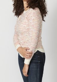 Suéter de punto en colores pastel con un patrón de ondas, con cuello redondo y puños acanalados. Combinado con jeans de mezclilla oscuros.