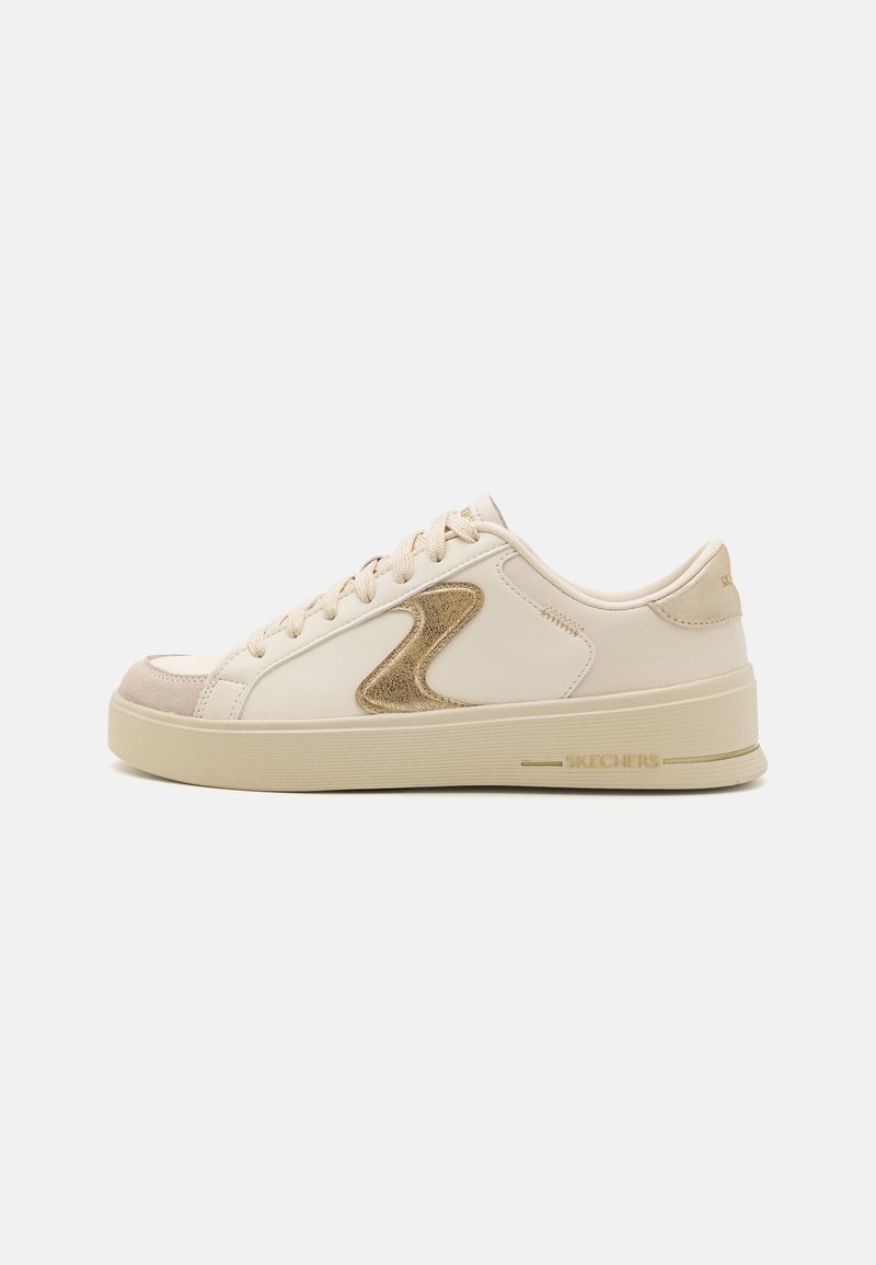 Sneaker beige a taglio basso con punta in suede marrone chiaro, logo ondulato dorato di lato, lacci beige e suola in gomma brandizzata su sfondo bianco.