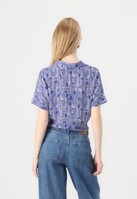Lilla kortermet skjorte med hvit abstrakt bølgete mønster, laget av bomull, rund hals, og avslappet passform, kombinert med blå høyhåndte jeans.