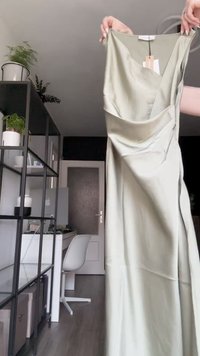 Vestido de cetim verde-claro com um design drapeado e decote em V profundo, com detalhes laterais e textura suave. Etiqueta visível no pescoço.