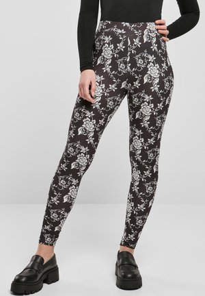 Svarta leggings med blommönster i vitt. Högmidjade med en slät textur och kroppsnära passform. Kombineras med kraftiga svarta skor.