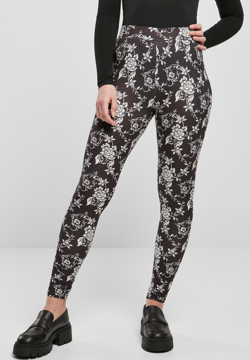 Svarta leggings med blommönster i vitt. Högmidjade med en slät textur och kroppsnära passform. Kombineras med kraftiga svarta skor.