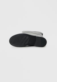 Black rubber boot with a textured sole, smooth upper, rounded toe, and a mid-calf height. Features grooves for traction.