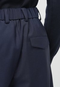 Calças azul marinho com cintura elástica, apresentando um bolso traseiro com aba. O tecido parece suave com um corte ajustado.