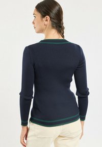 Pull côtelé marine à manches longues, accents de rayures vertes au niveau de l'encolure et des poignets, coupe ajustée et texture douce.