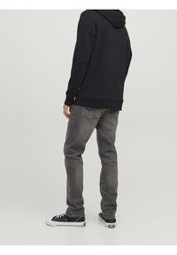 Felpa nera con cappuccio dal fit rilassato e polsini a coste, abbinata a jeans grigi scoloriti e sneakers nere con suola bianca.