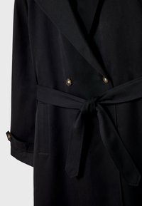 Schwarzer doppelreihiger Trenchcoat aus glattem Stoff, mit gebundenem Taillengürtel, zwei Knöpfen und hochgerollten Ärmelabschlüssen mit Knopfakzenten.