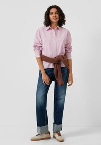 Striped pink button-up shirt, paired with blue jeans, and light beige sneakers. Brown knit sweater tied at the waist. Casual outfit.