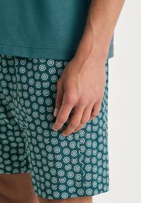 Turquoise t-shirt en gestreepte shorts met hexagonale motieven in teal, wit en donkerblauw, gemaakt van een lichtgewicht stof.