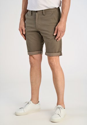 Pantaloncini di cotone verde oliva con orli arrotolati, due tasche frontali, chiusura con bottone e tessuto con motivo testurizzato. Indossati con sneaker bianche.