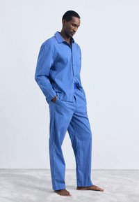 Set de pijamale în carouri albastre, realizat dintr-un material moale, compus dintr-o cămașă cu nasturi și guler deschis, împreună cu o pereche de pantaloni lejerași asortați.